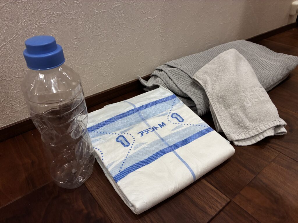 園芸用シャワーキャップを取り付けた500mlのペットボトルと、開いて使う紙オムツ、バスタオル